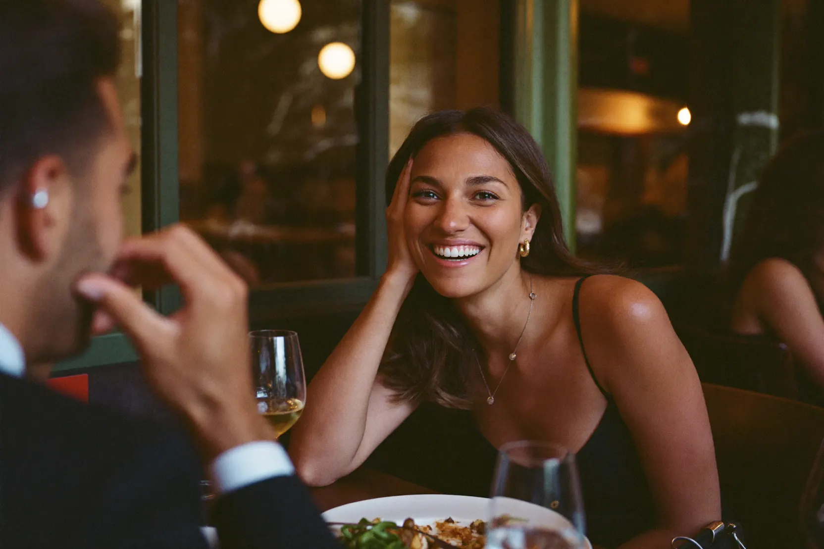 A woman smiling across a restaurant table, from the seat opposite her